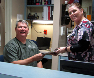 Picture of a male Physician and female Nurse behind a desk smiling.